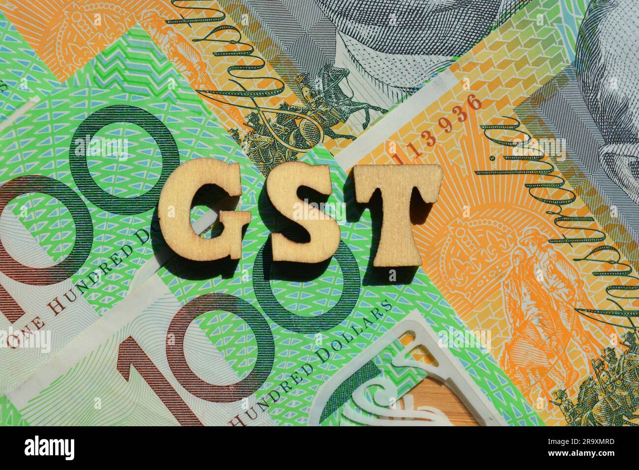 GST, abbreviation for Goods and Services Tax in wooden alphabet letters isolated on background of Australian hundred dollar banknotes Stock Photo