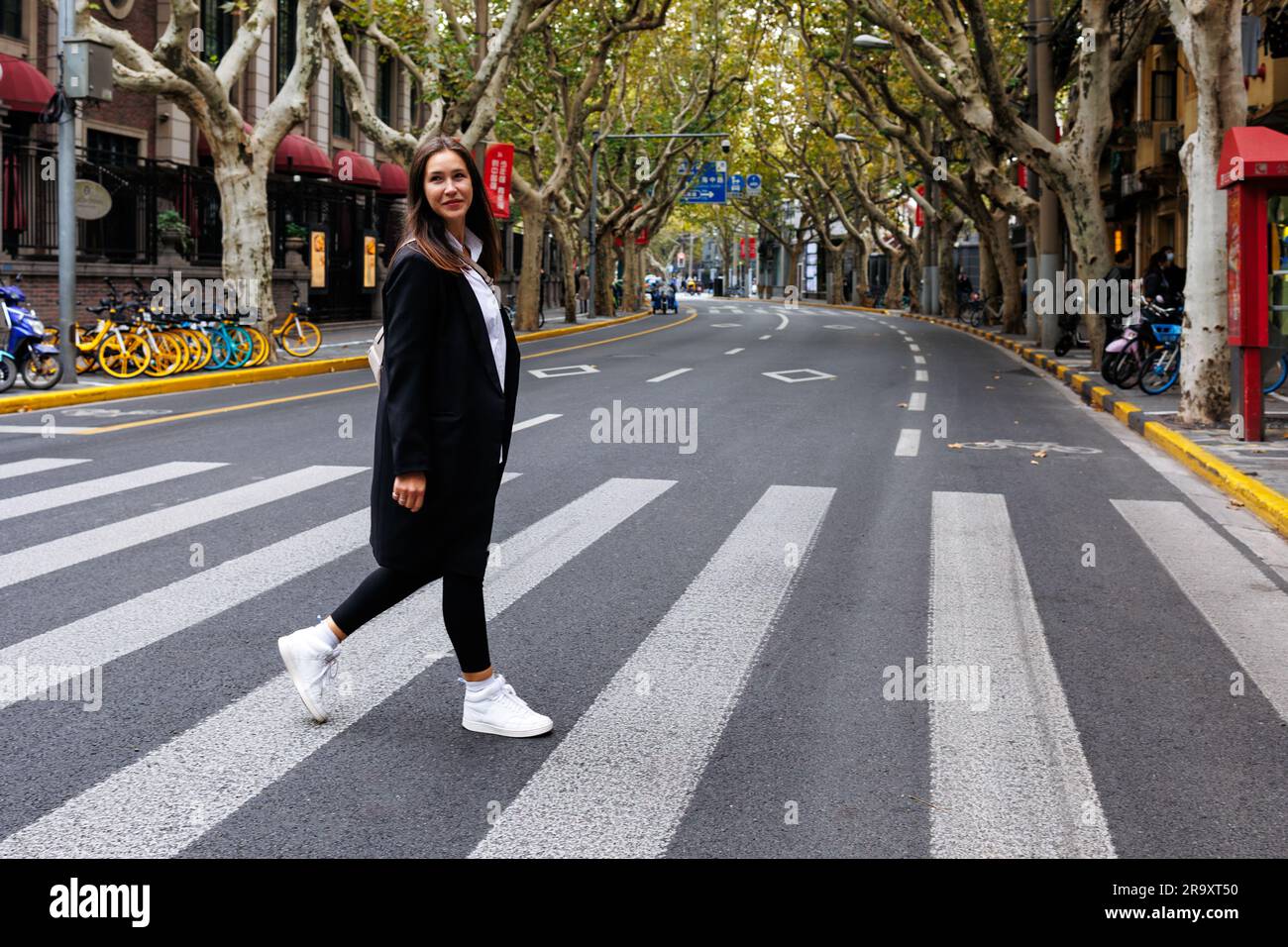 Smiling young woman crossing the street at a pedestrian crosswalk in ...