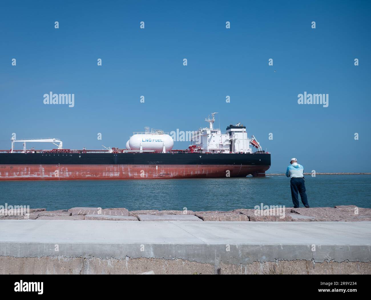 PORT ARANSAS, TX - 26 FEB 2023: Fisherman fishing at the South Jetty at the Gulf of Mexico in Port Aransas, Texas, as a tanker ship sails on the water Stock Photo