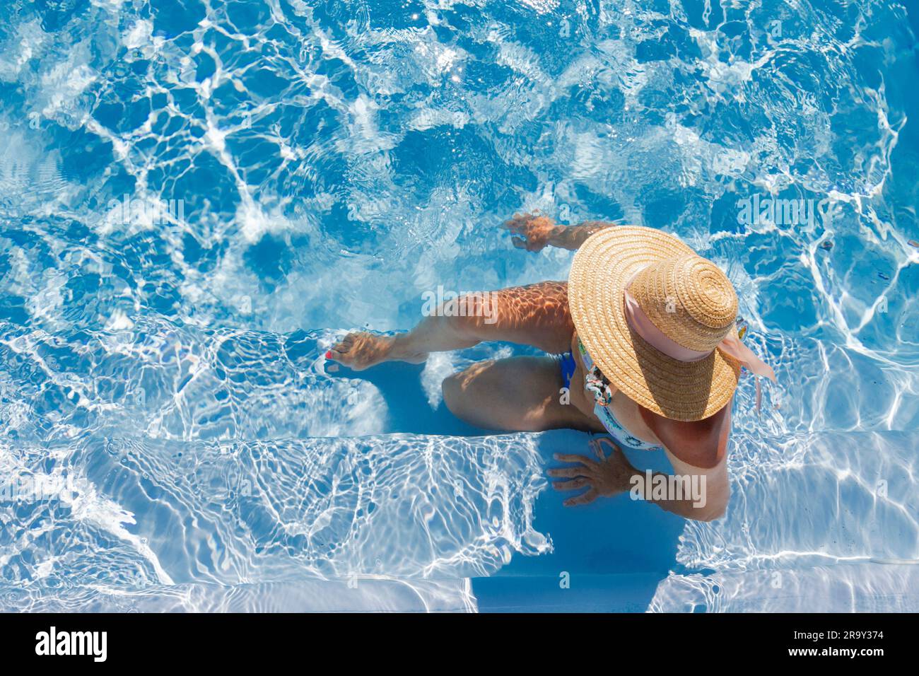 A woman sitting in the pool wearing a sun hat while sunbathing Stock ...
