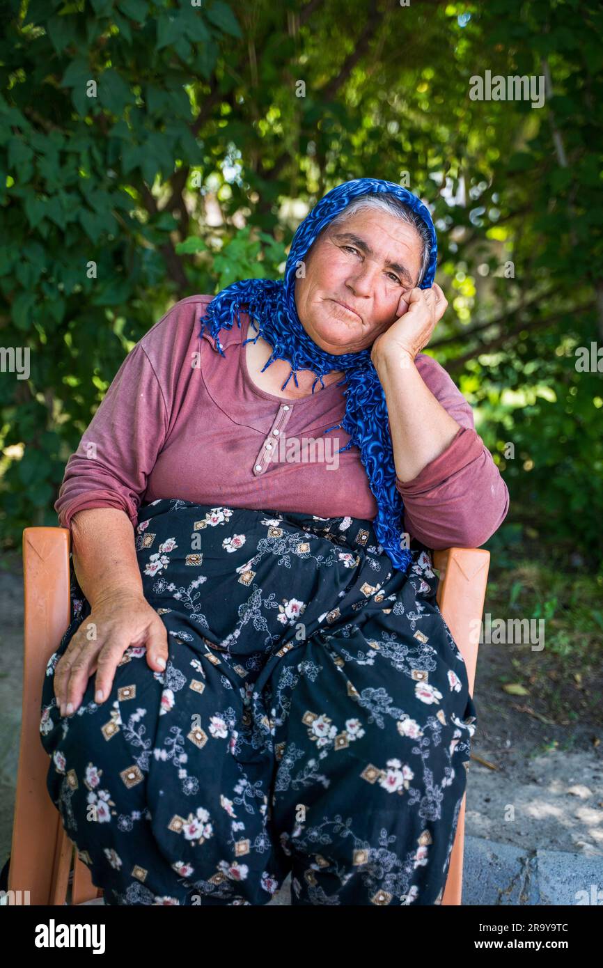 Anatolia, Turkey - September 12, 2021: An old turkish woman wearing scarf covering head in traditional wear sitting on a chair outdoors Stock Photo