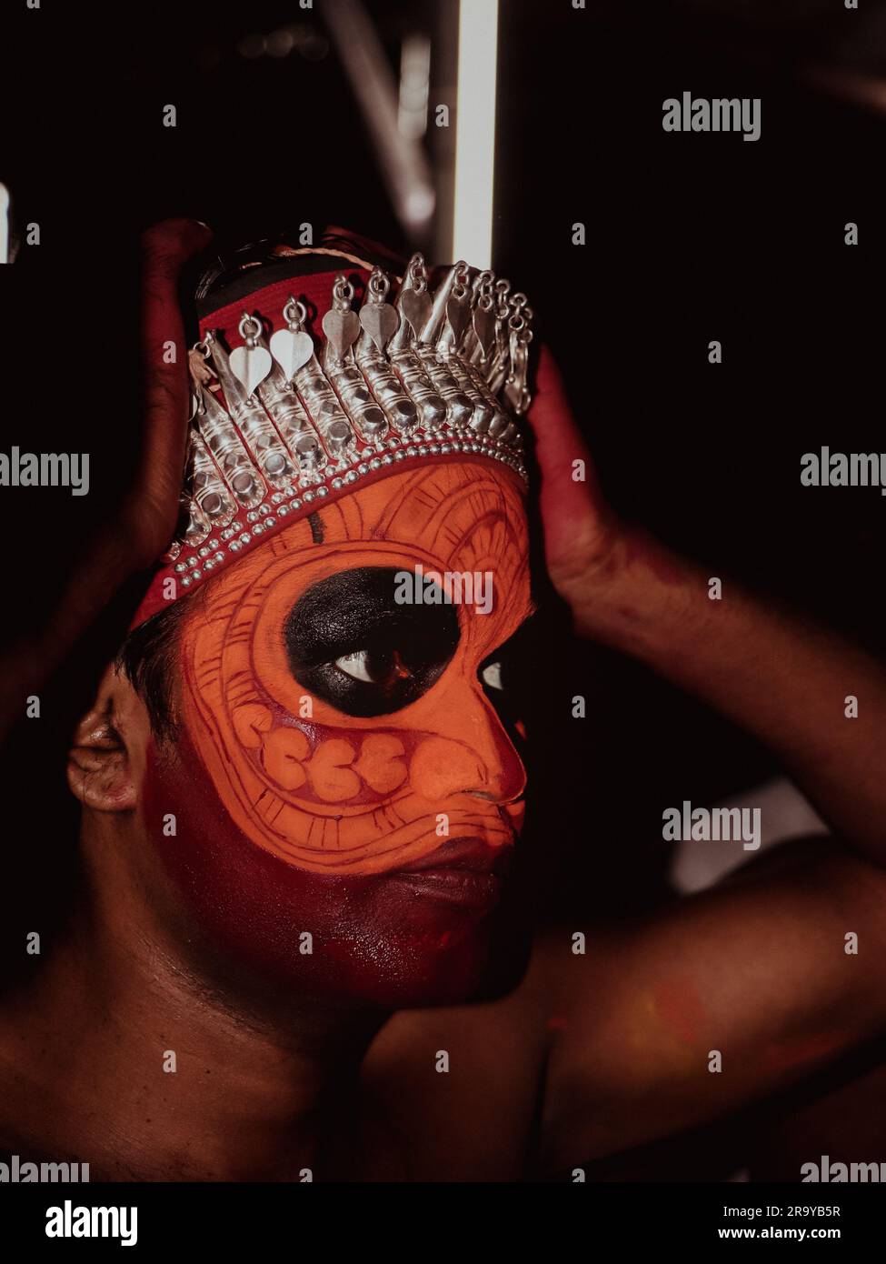 a closeup portrait of an artist with face paint makeup who performs theyyam, a traditional dance and art form that celebrates and worship hindu cultur Stock Photo
