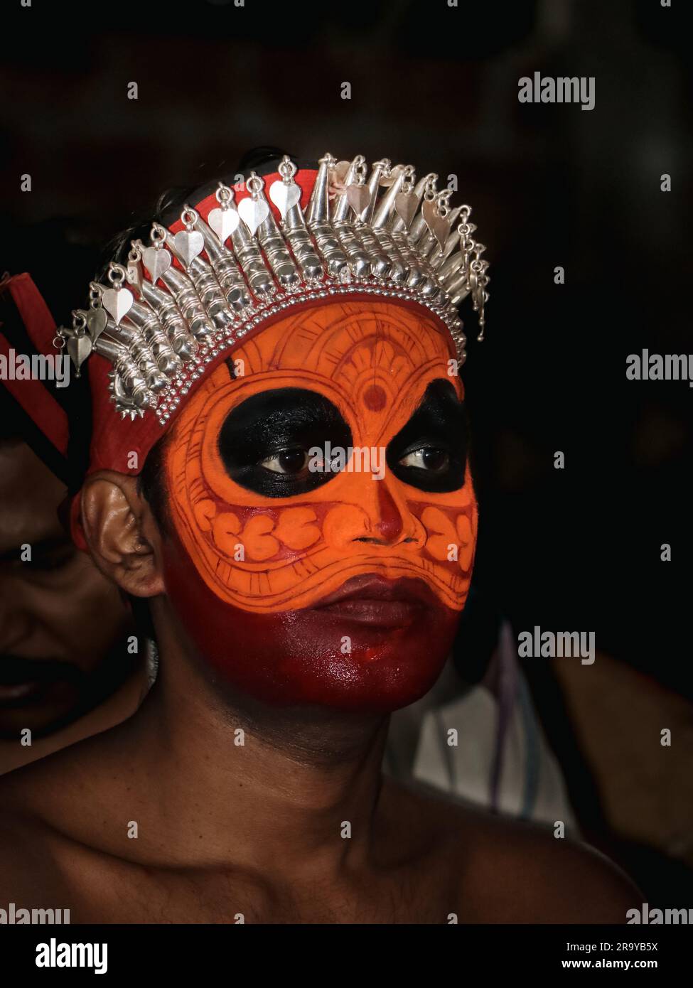 a closeup portrait of an artist with face paint makeup who performs theyyam, a traditional dance and art form that celebrates and worship hindu cultur Stock Photo