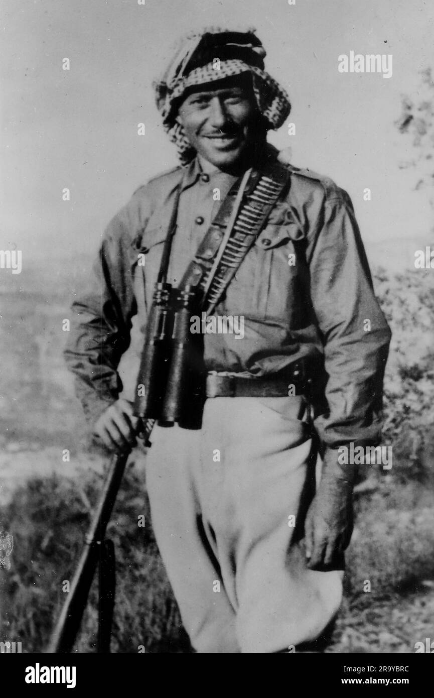 An armed Arab with binoculars hanging from his neck, part of a group ...