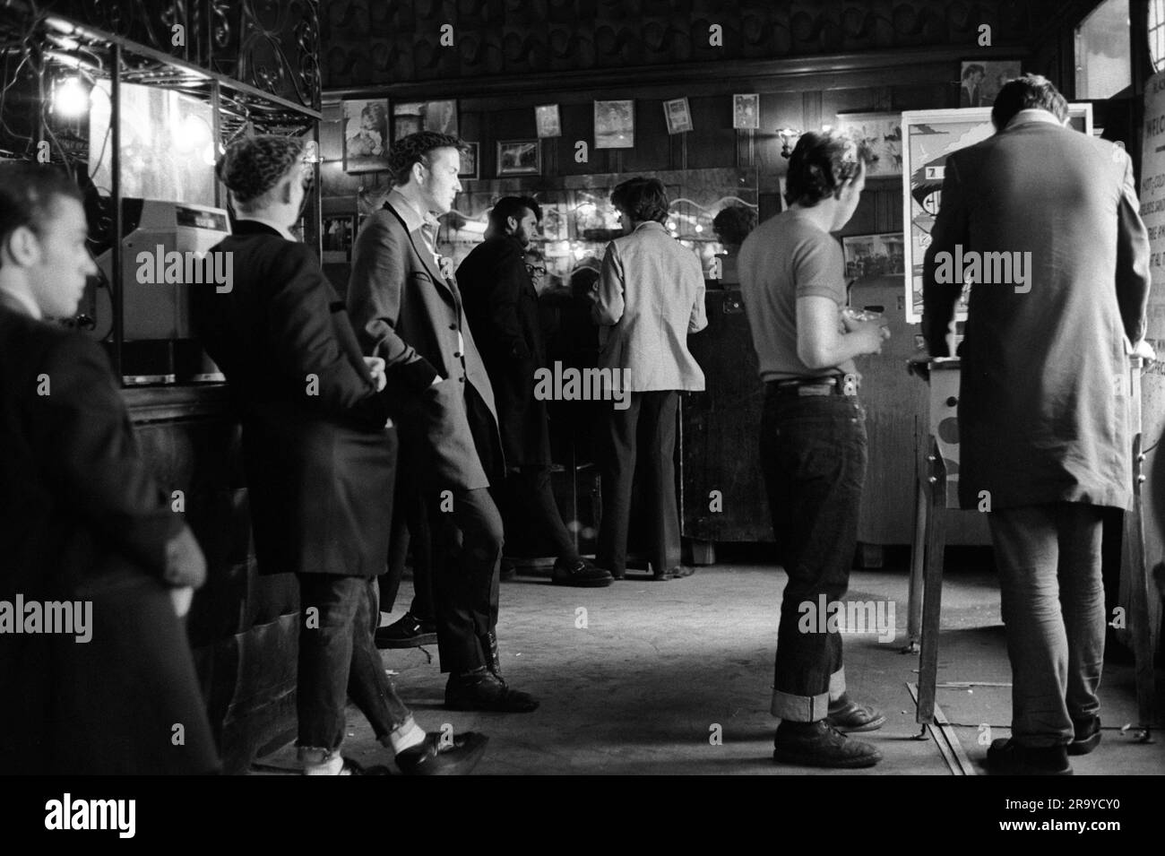 Teddy Boys 1970s. Playing a pinball machine at The Black Raven in Bishopgate Street, a group of Teddy Boys in long drape coats hang out. Moorgate, London, England circa 1975. 1970s UK HOMER SYKES Stock Photo