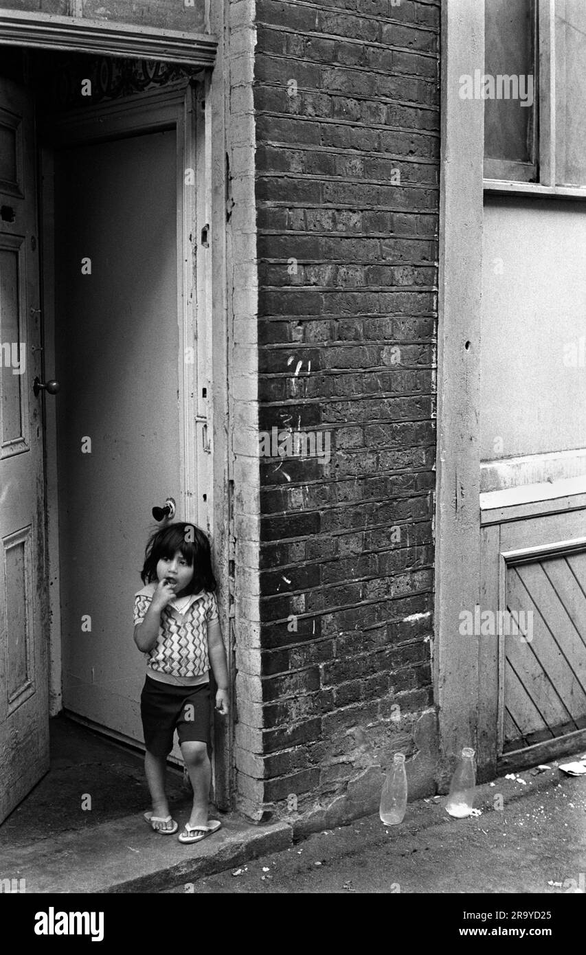 East End London 1970s, the Peabody Estate in Princess Street a multiracial block of flats in 1970s Britain.  A new immigrant child stands in the doorway to the block of flats. Two empty glass milk bottles are outside on the pavement. Whitechapel, London, England circa 1975. 70s UK HOMER SYKES Stock Photo