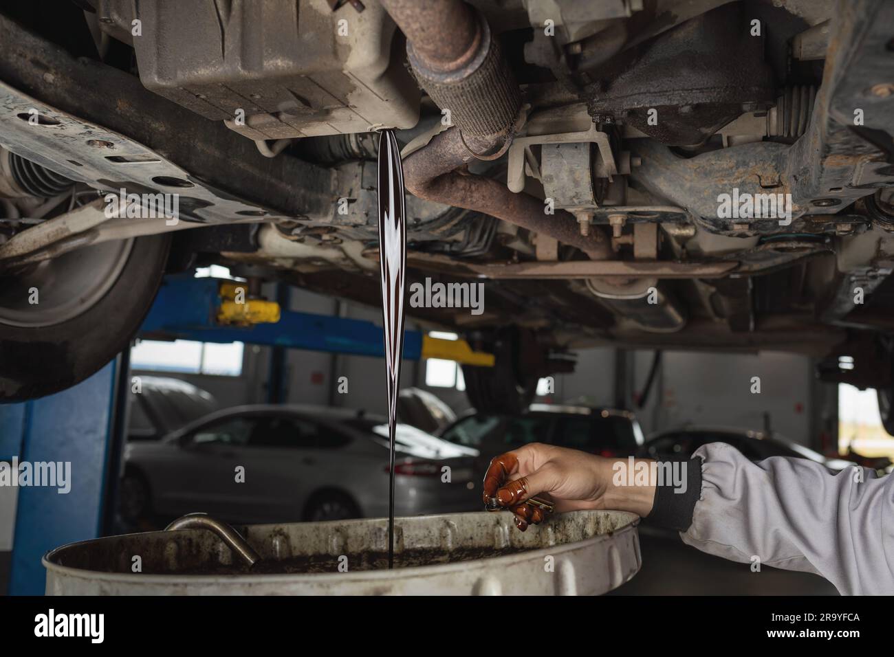 Auto mechanic drains old used engine oil at a service station, scheduled service maintenance of a passenger car Stock Photo