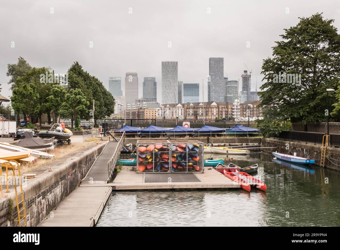 Colourful canoes and boats on Shadwell Basin with the skyscrapers of Docklands and Canary Wharf in the background, London, England, U.K. Stock Photo