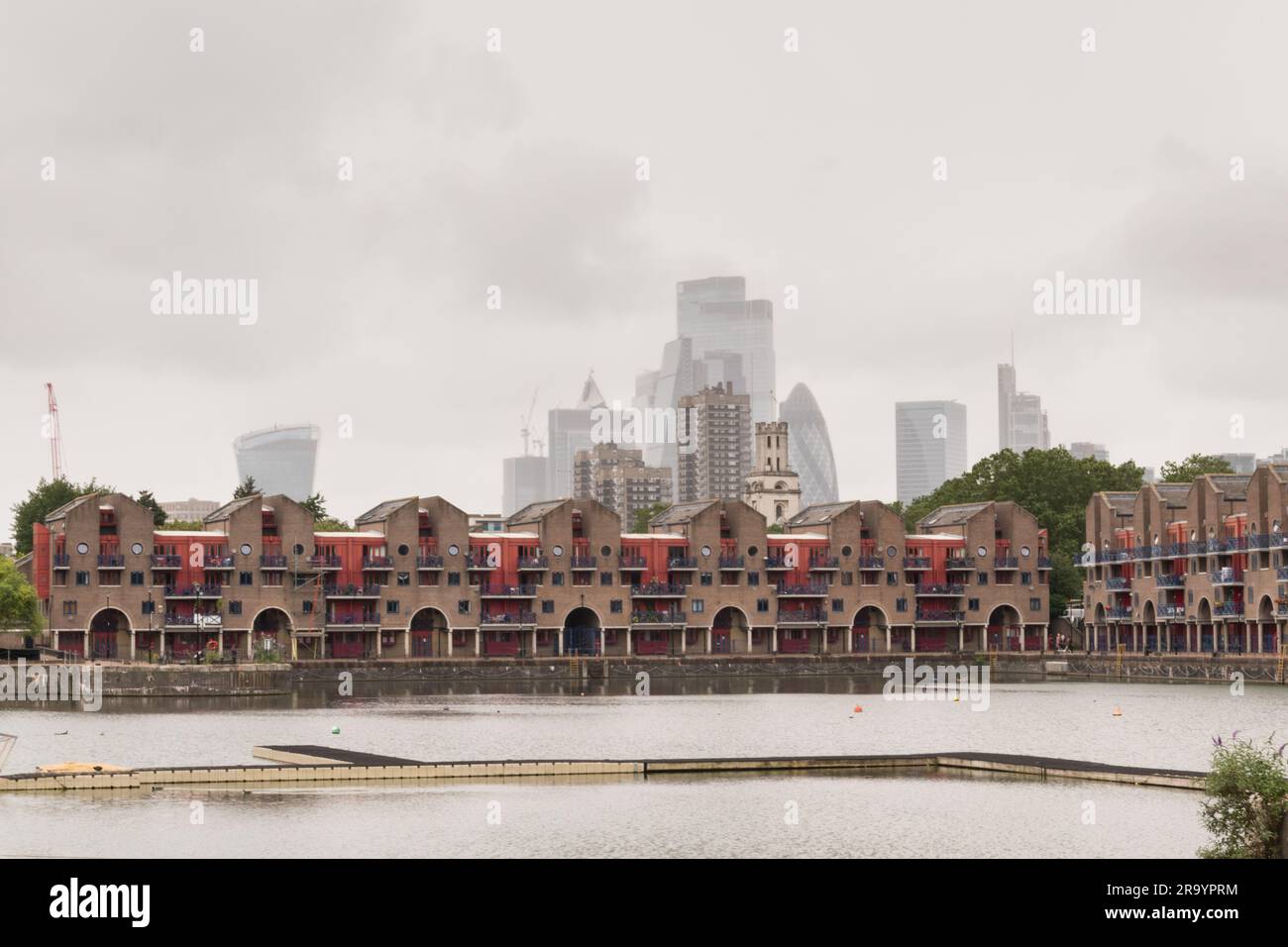Property on Shadwell Basin, and a grey and gloomy City of London skyline in the background, London, England, U.K. Stock Photo