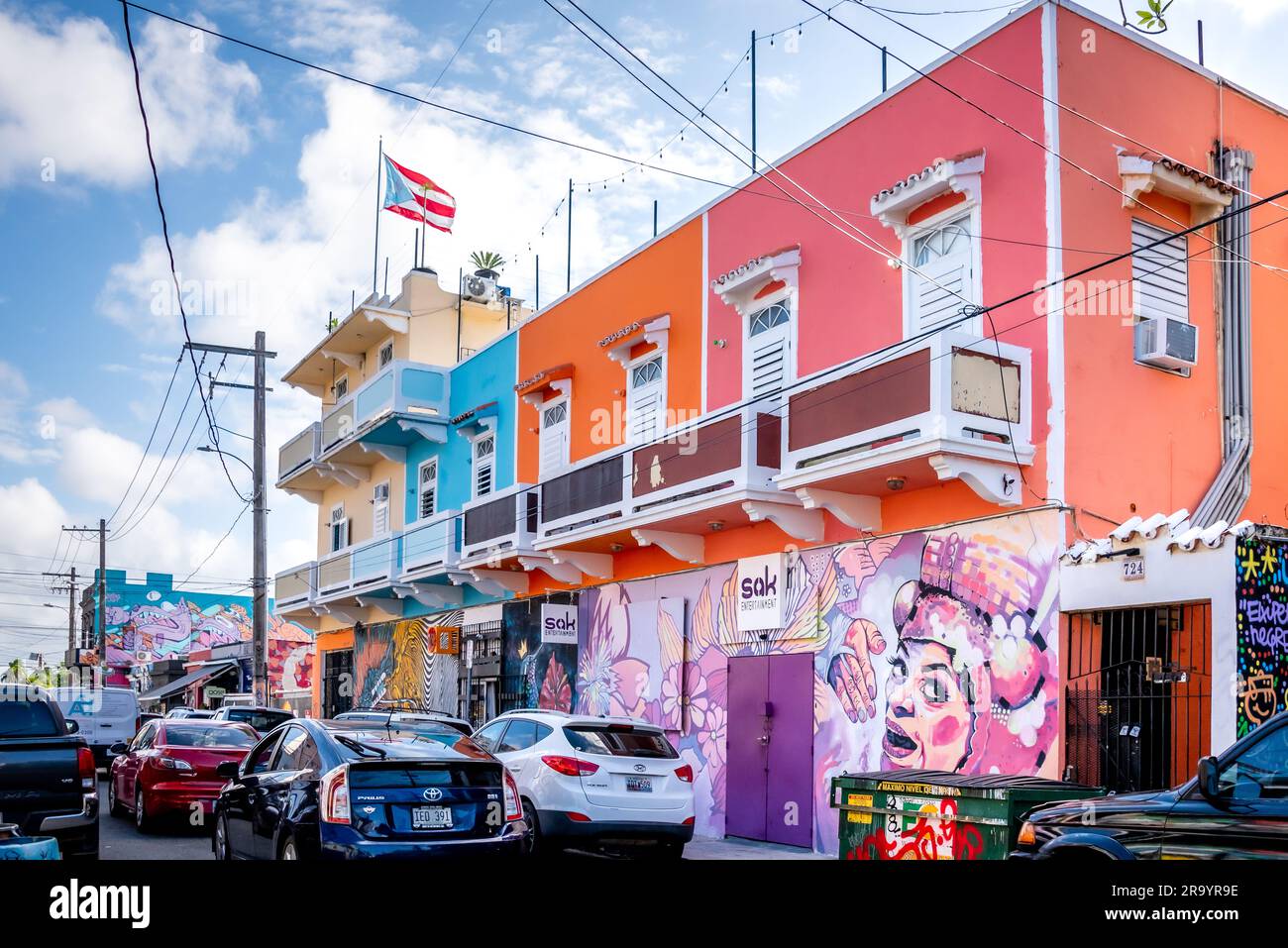 A colorful and freshly painted row of buildings in San Juan, Puerto Rico, with murals on ground level of a busy street with cars and Puerto Rico flag. Stock Photo