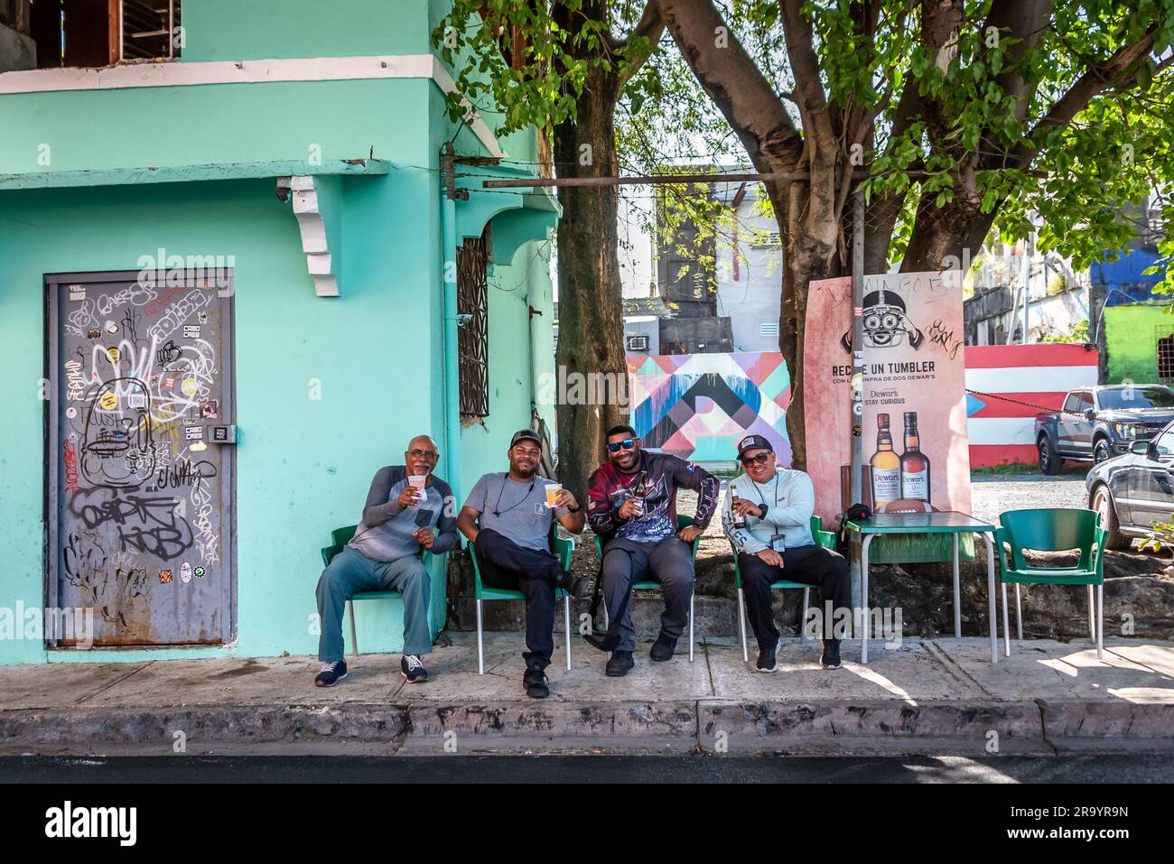 Friends (men) gather for a drink after work at an informal sidewalk pub with green chairs in the Santurce neighborhood of San Juan, Puerto Rico. Stock Photo