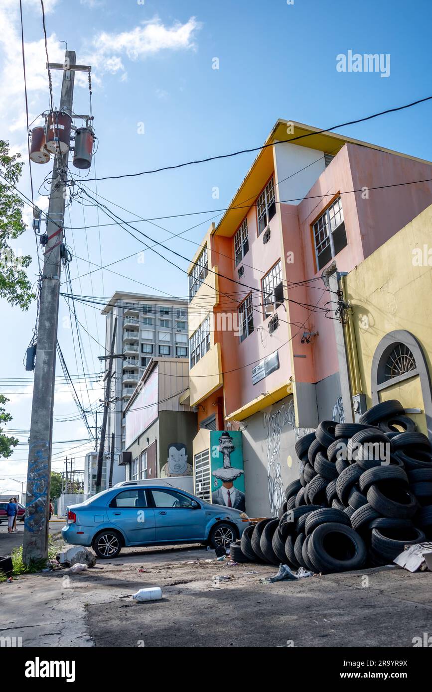 Neighborhood street in Santurce distric of San Juan, Puerto Rico, view of sidewalk with parked car and pile of tires outside apartment building. Stock Photo