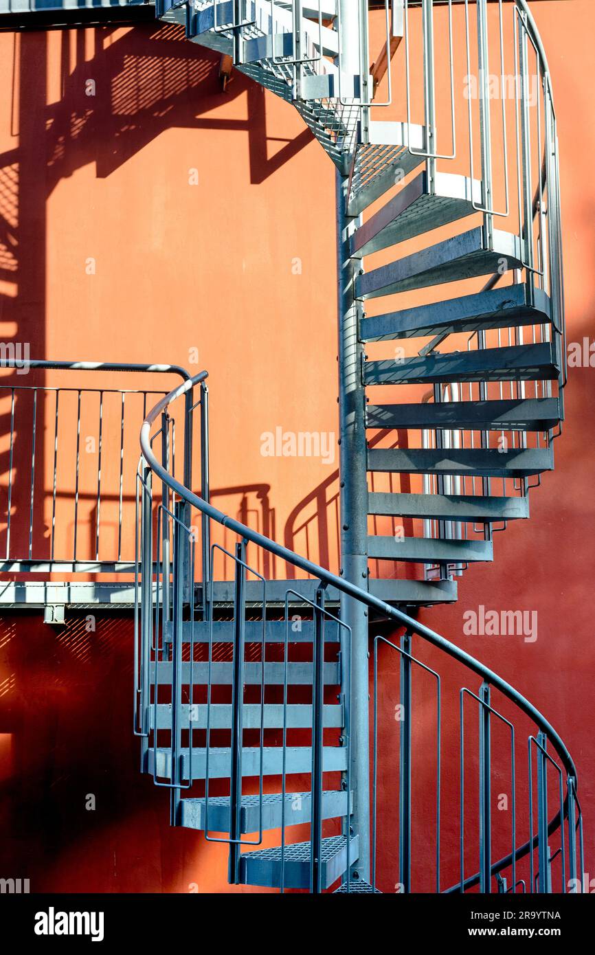 Staircase and shadow. Gray metal stairs next to the wall of the orange building. Stock Photo