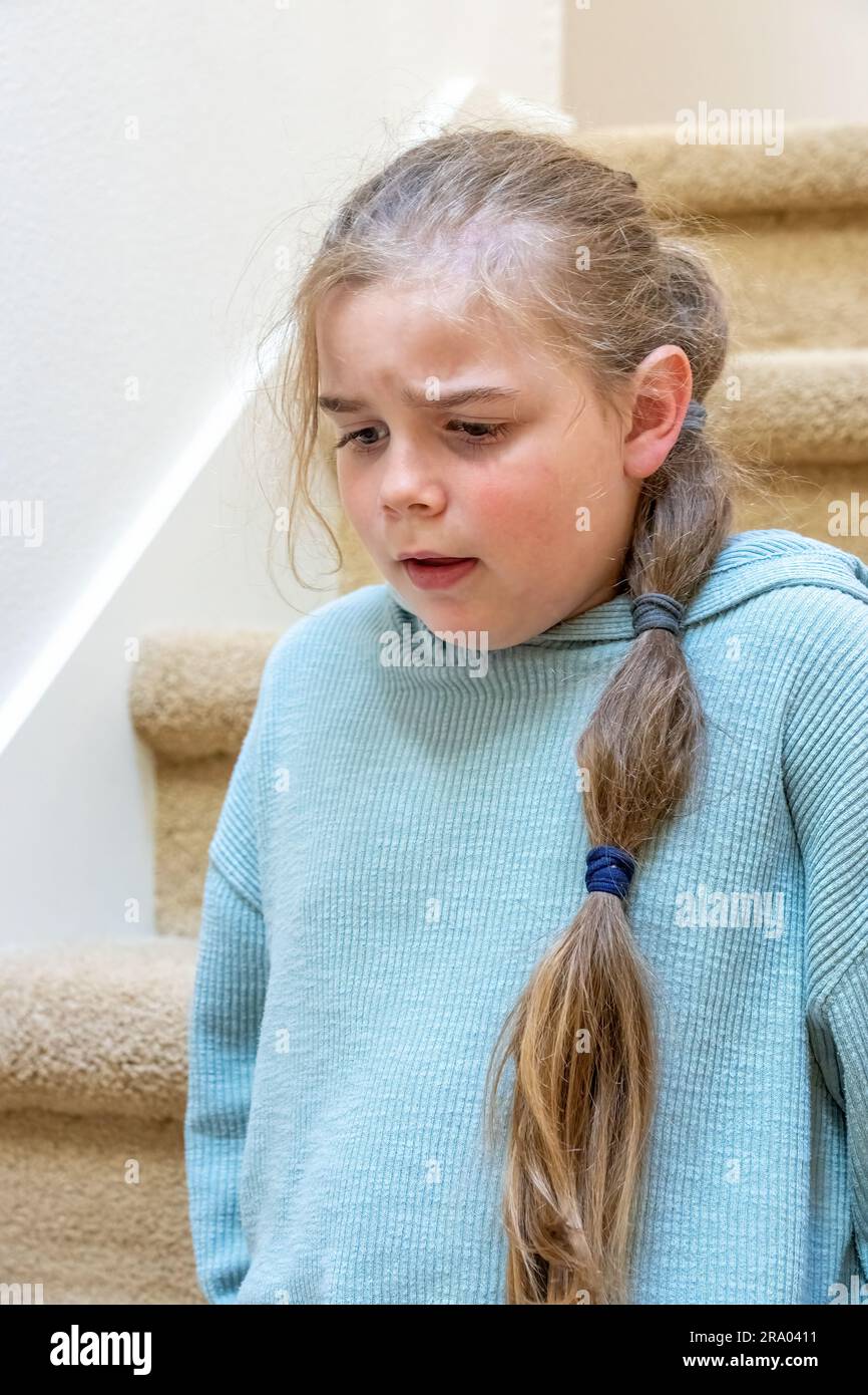 Portrait of a very unhappy 7 year old girl sitting on a staircase. (MR) Stock Photo