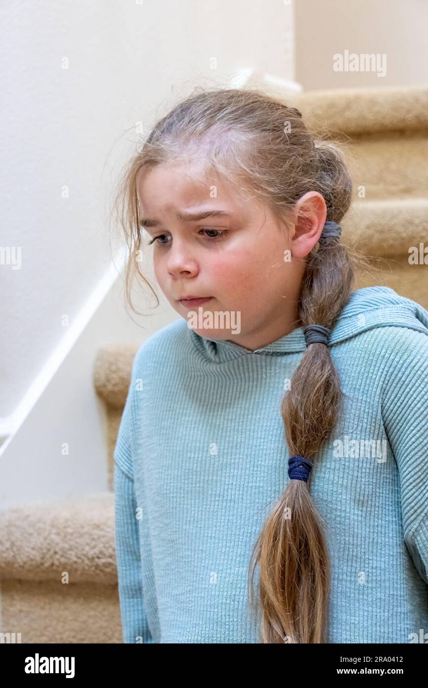 Portrait of a very unhappy 7 year old girl sitting on a staircase. (MR) Stock Photo