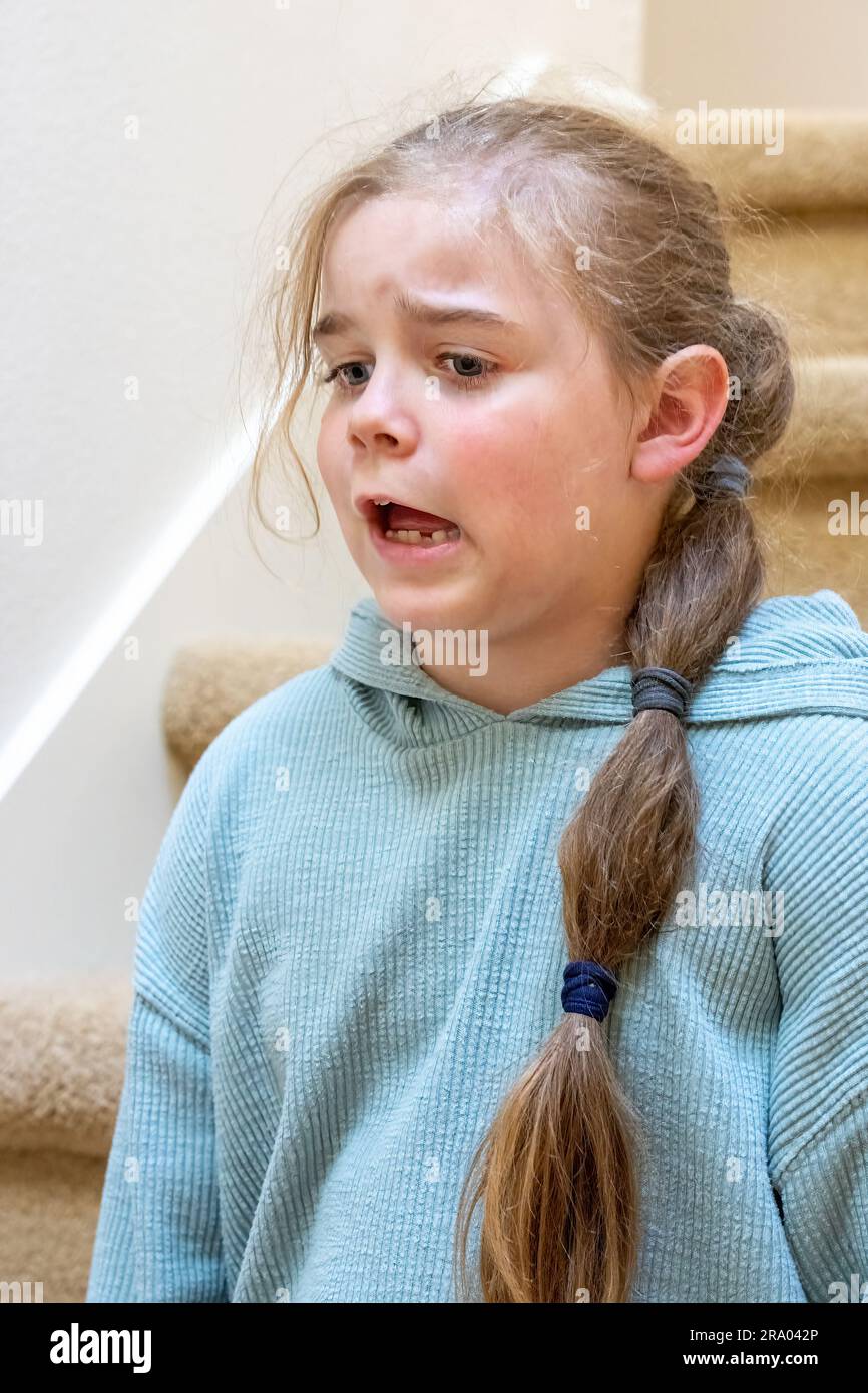 Portrait of a very unhappy 7 year old girl sitting on a staircase. (MR) Stock Photo