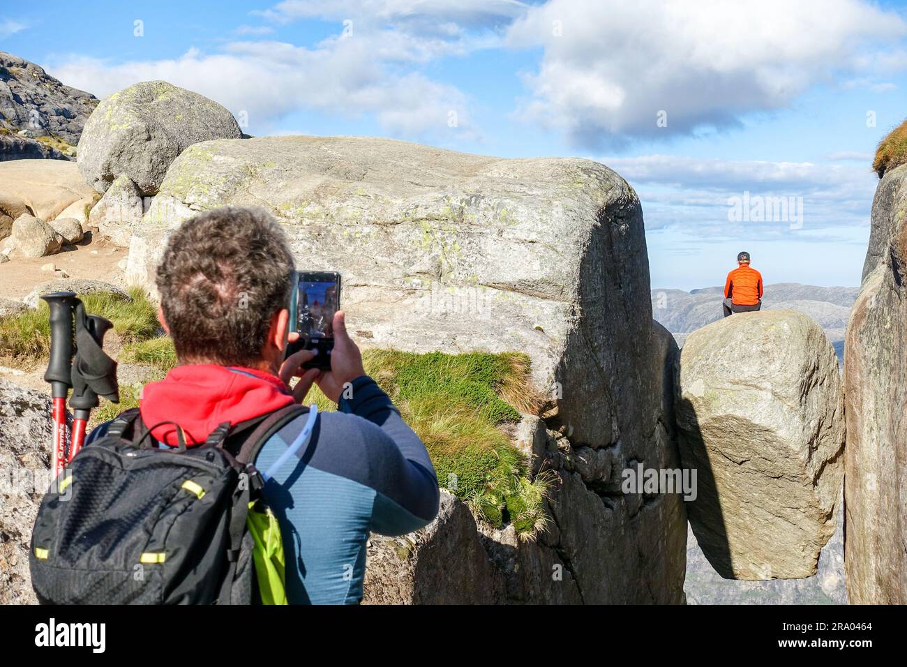 Hiker taking a photo of another hiker sitting on the Kjerag boulder, Norway Stock Photo