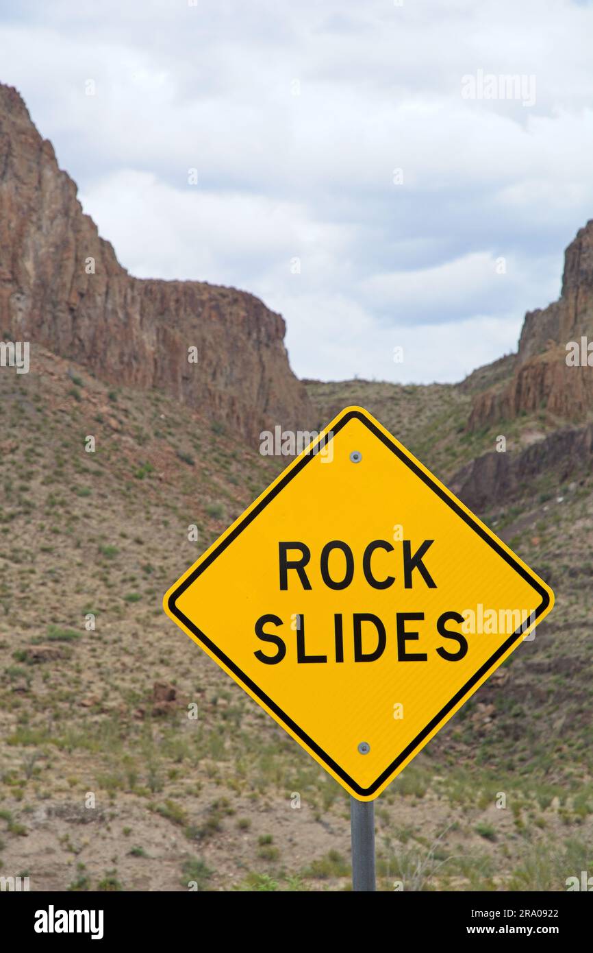 Rock slide road warning sign set before steep canyon walls in the