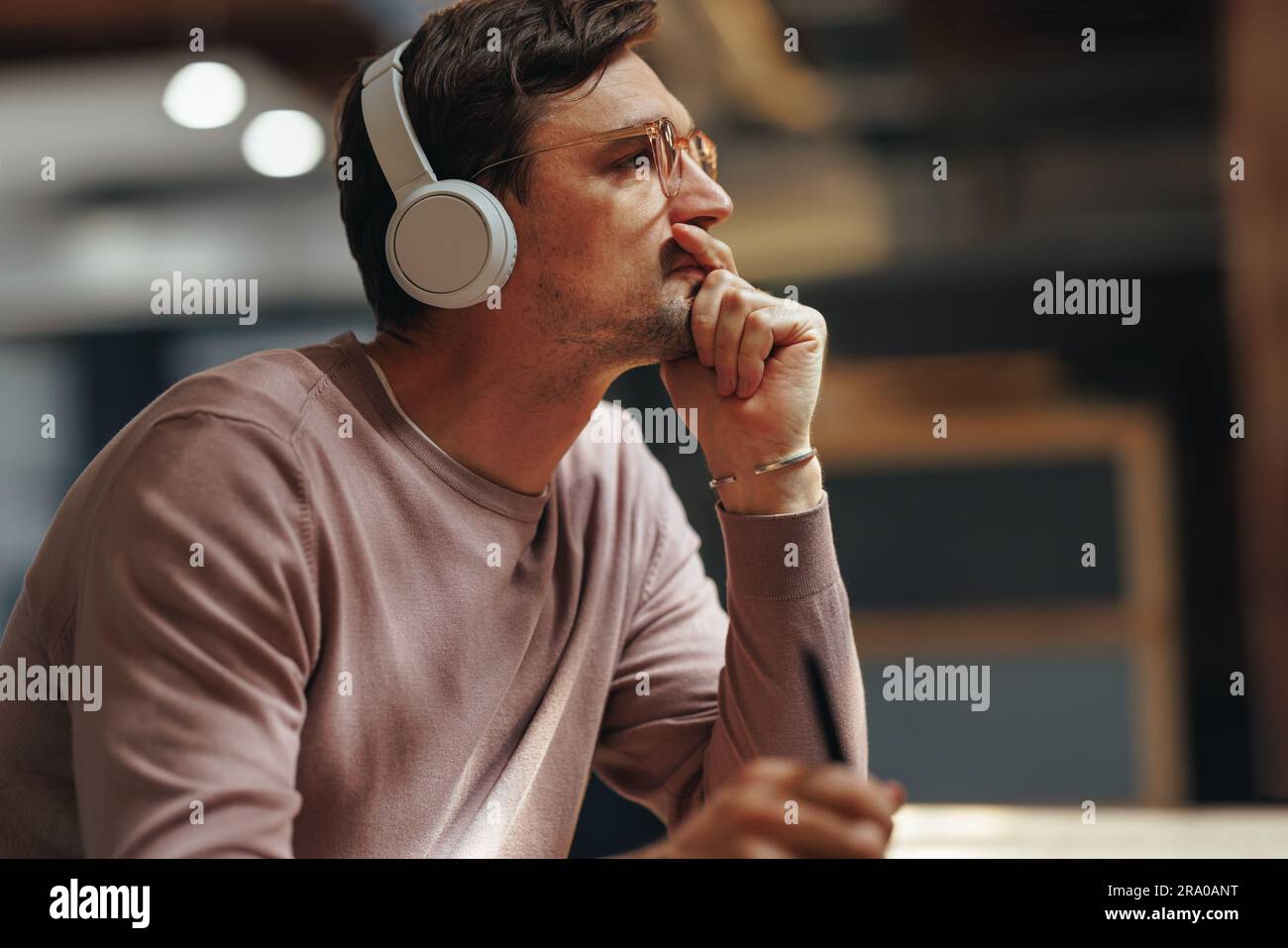 Designer thinking about his project while sitting in a cafe. Male graphic design professional wearing wireless headphones. Stock Photo