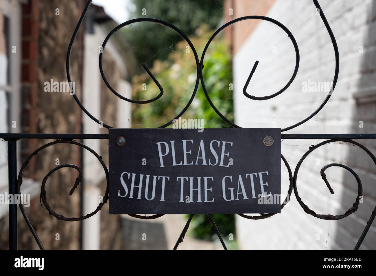 Polite notice reminding people to shut the gate mounted on an ornate metal gate. Stock Photo
