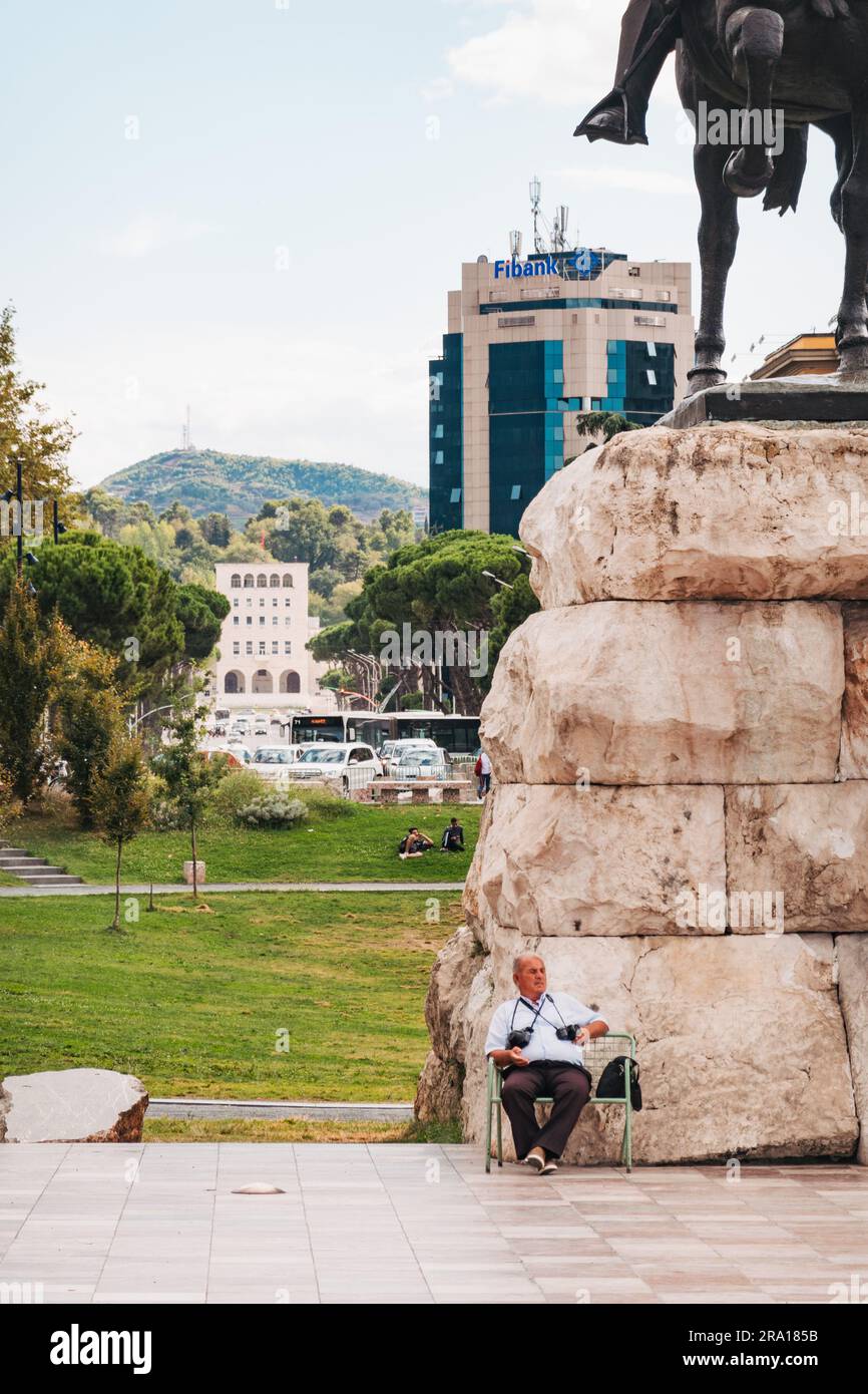 a man sits on front of the Skanderbeg Monument – a national hereo who fought off the Ottomans – in Skanderbeg Square, Tirana, Albania Stock Photo