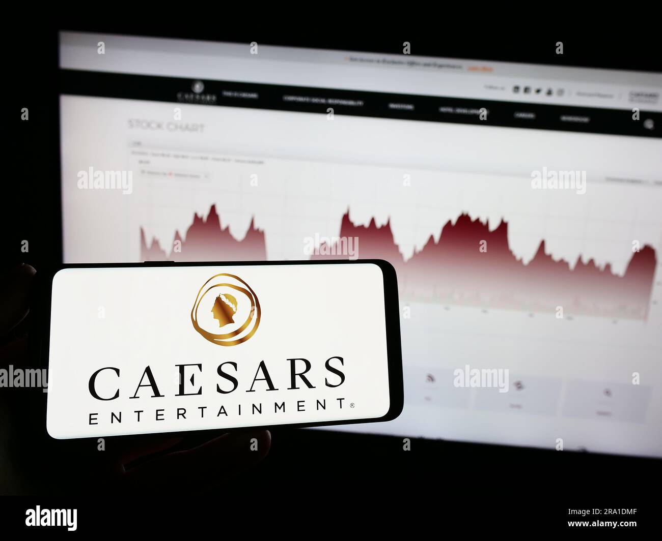 Person holding mobile phone with logo of American company Caesars Entertainment Inc. on screen in front of web page. Focus on phone display. Stock Photo