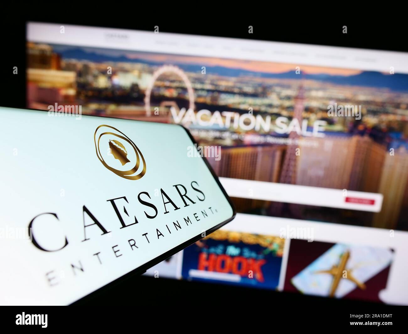 Mobile phone with logo of American company Caesars Entertainment Inc. on screen in front of website. Focus on center-right of phone display. Stock Photo