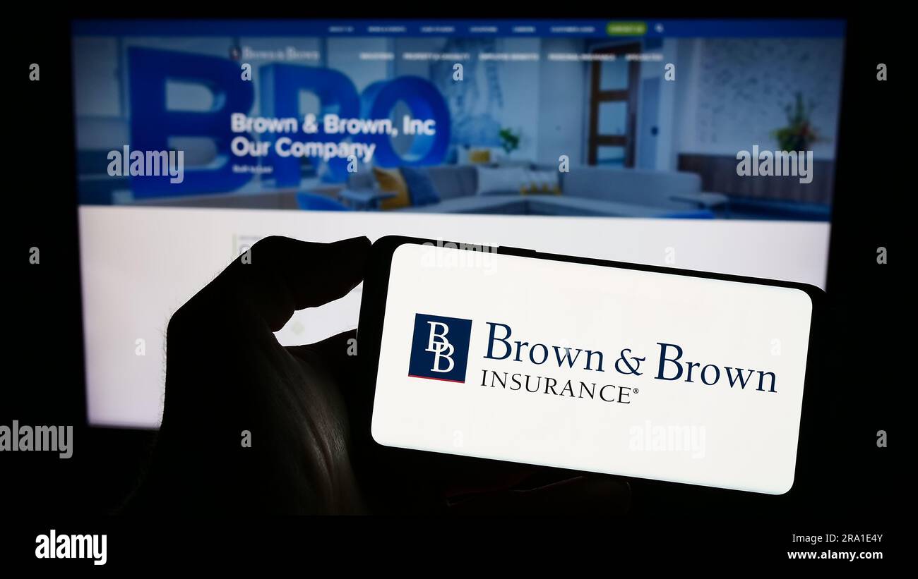 Person holding smartphone with logo of US insurance company Brown and Brown Inc. on screen in