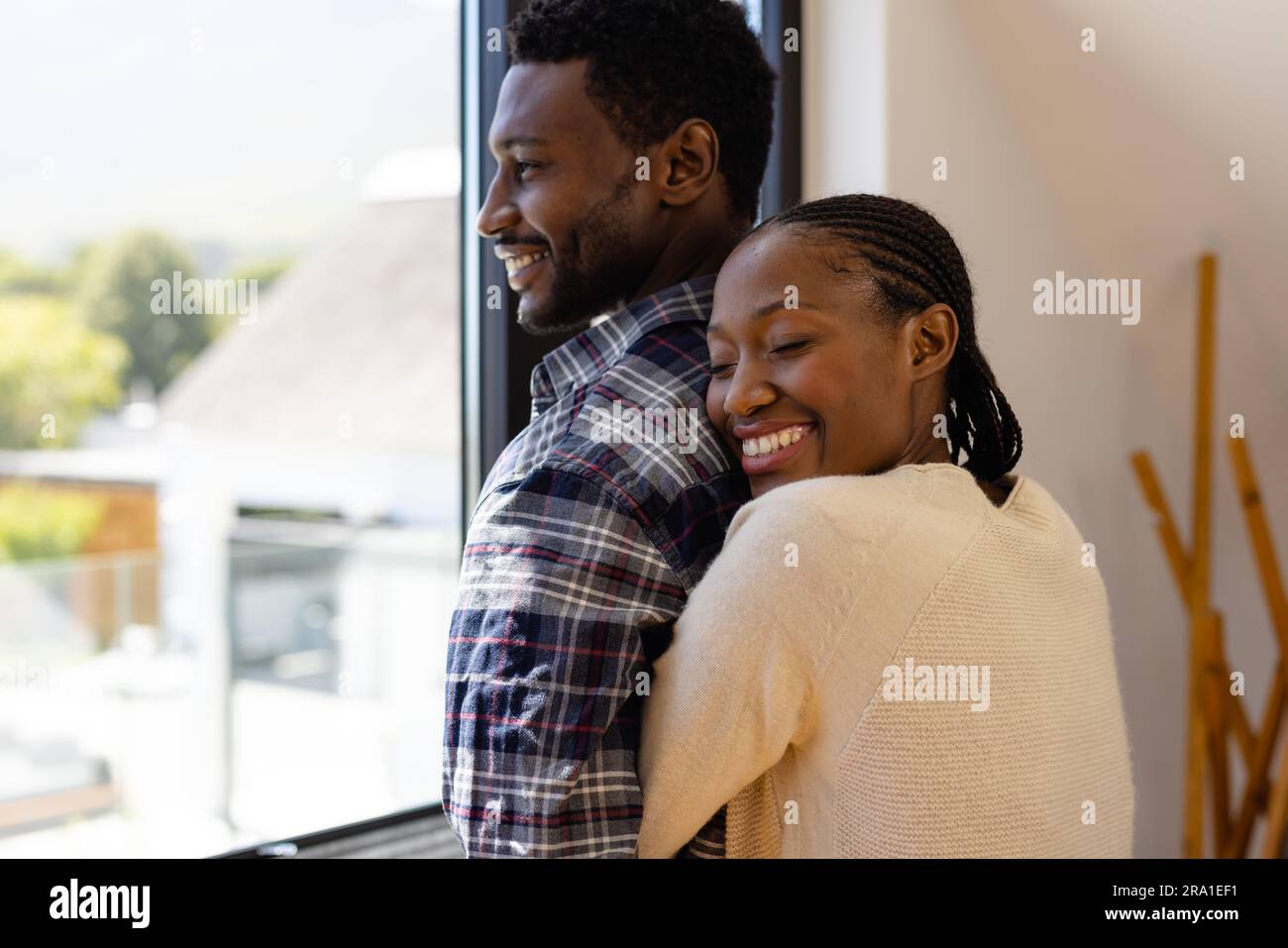 Happy african american couple hugging by window at home Stock Photo - Alamy