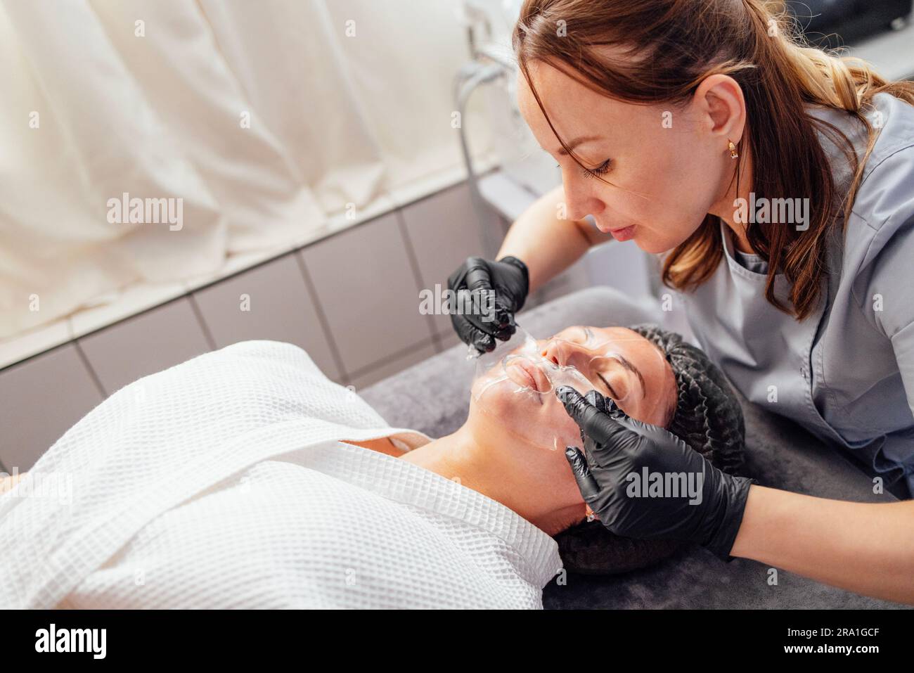 Young Cosmetologist Woman In Black Gloves Applies A Transparent Vitamin 