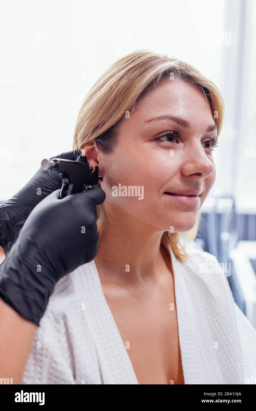 Close up of face of young blonde woman doing ear piercing procedure