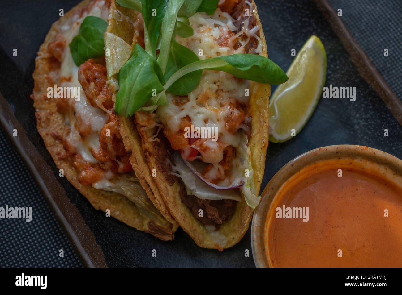 Flavorful Mexican-style tacos featuring succulent shrimp, tomatoes, cheese, chili, and onions, served with a side of hot and tangy Mexican sauce for a Stock Photo