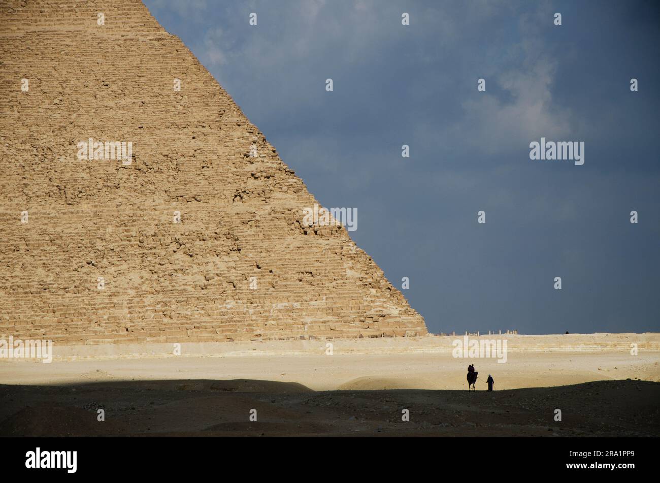 Lonely man and his camel travel through a desert to a pyramid Stock Photo