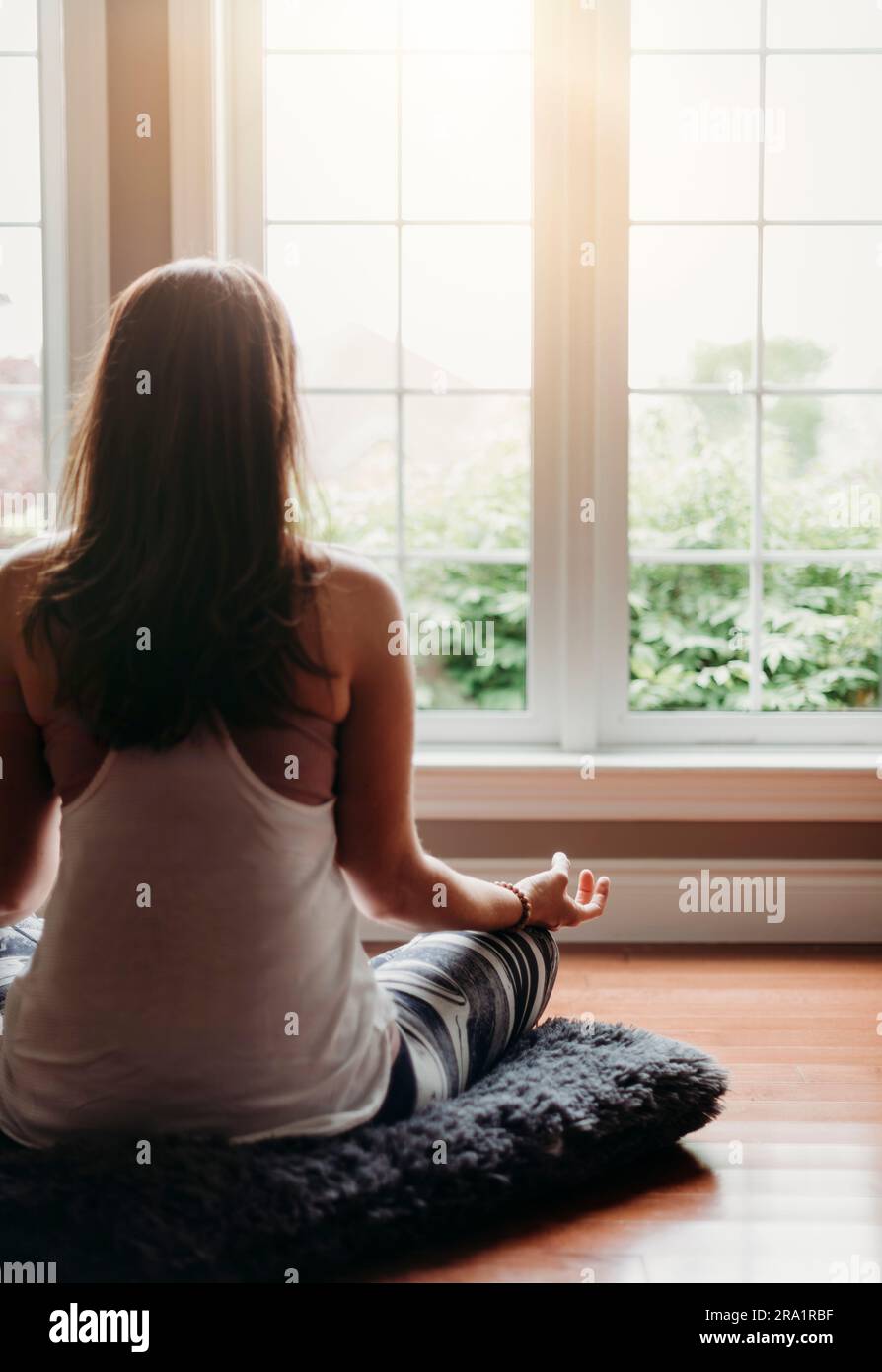 Woman sitting on the floor indoors meditating in front of windows Stock ...