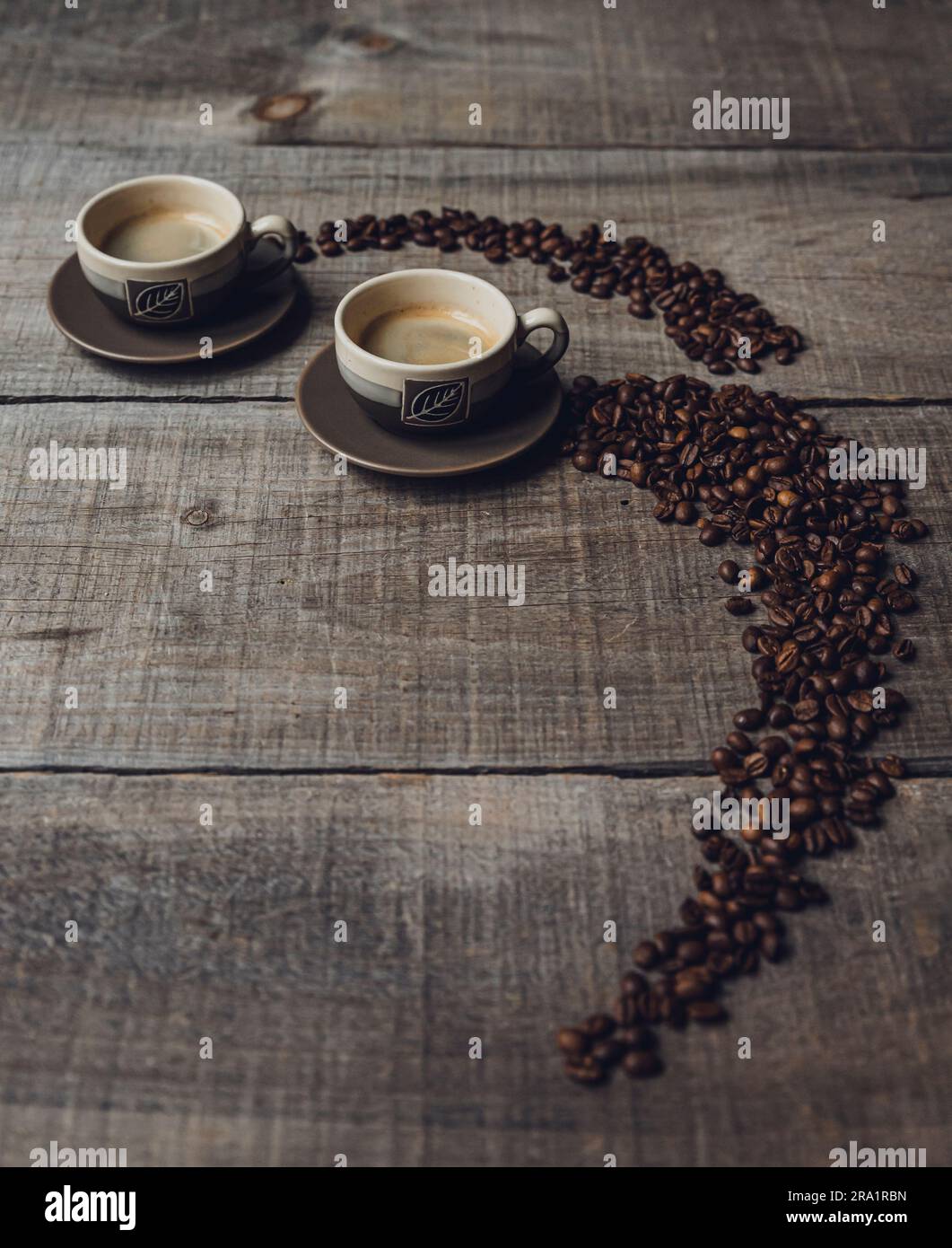 https://c8.alamy.com/comp/2RA1RBN/coffee-beans-leading-up-to-cups-of-espresso-on-a-wooden-table-2RA1RBN.jpg