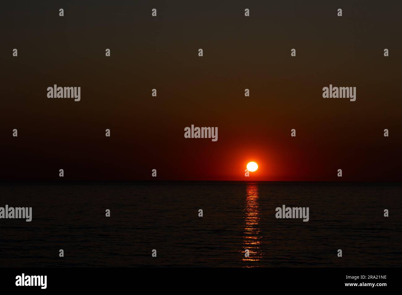 A large orange sun setting over a calm sea. Static shot taken during a cloudless evening. Image under exposed in purpose Stock Photo