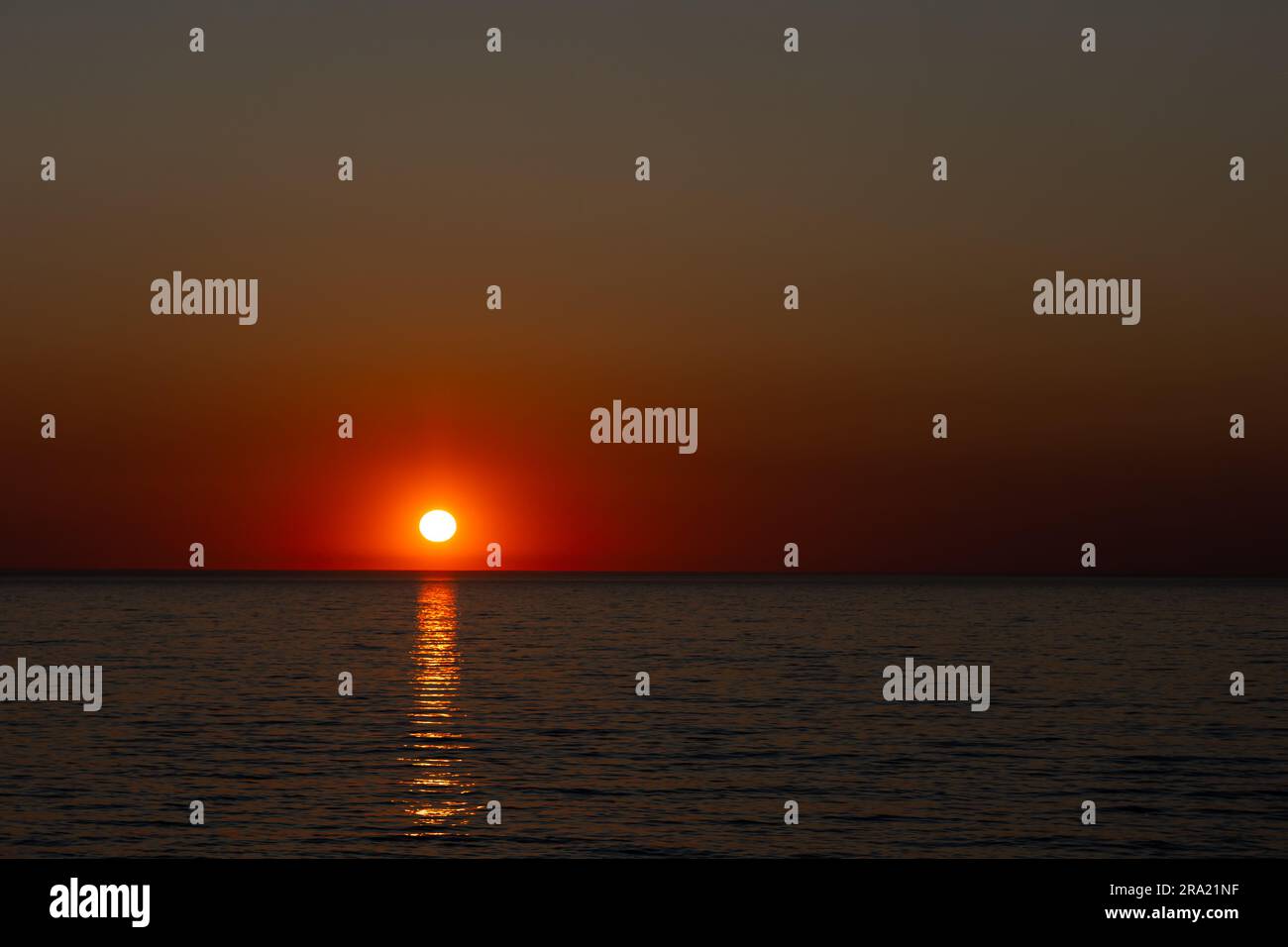 A large orange sun setting over a calm sea. Static shot taken during a cloudless evening. Image under exposed in purpose Stock Photo