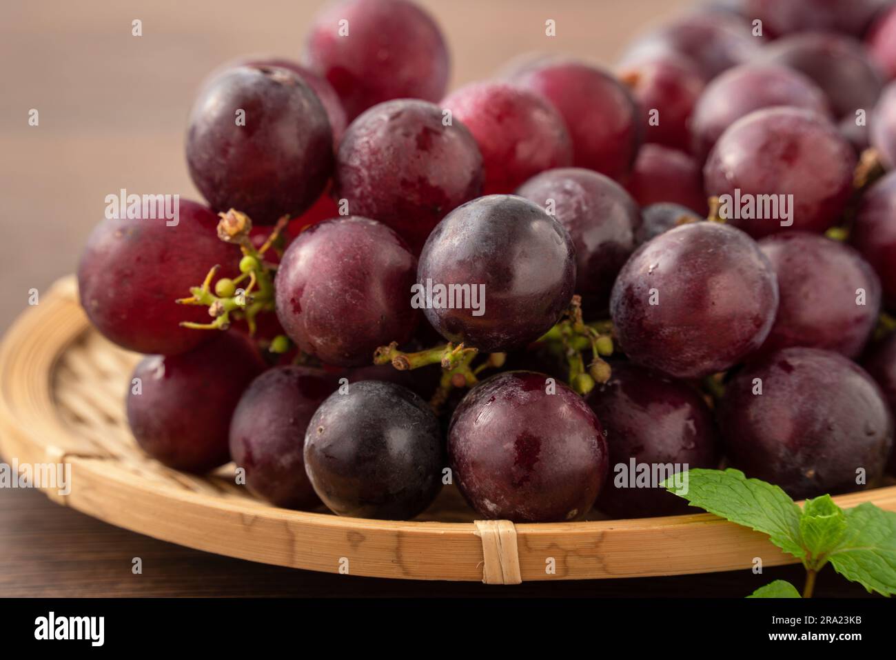 Delicious bunch of purple grapes fruit on a tray over wooden table background. Stock Photo