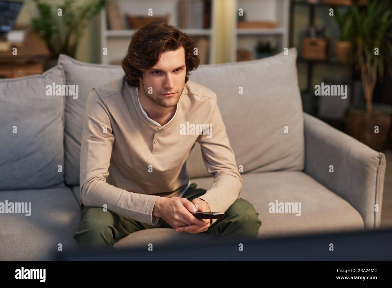 Portrait of young man watching TV at home sitting on sofa in cozy green interior, copy space Stock Photo