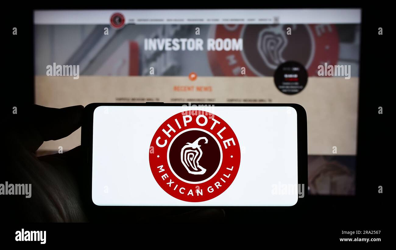 Person holding cellphone with logo of US company Chipotle Mexican Grill Inc. on screen in front of business webpage. Focus on phone display. Stock Photo