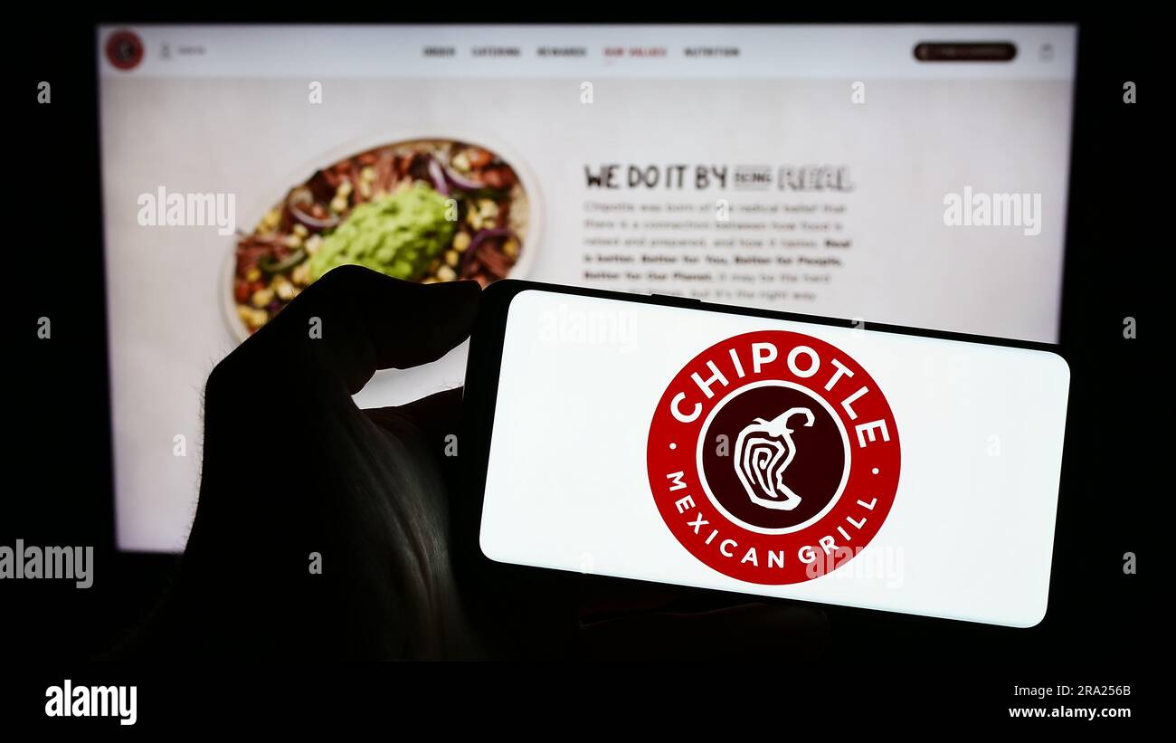 Person holding smartphone with logo of US company Chipotle Mexican Grill Inc. on screen in front of website. Focus on phone display. Stock Photo
