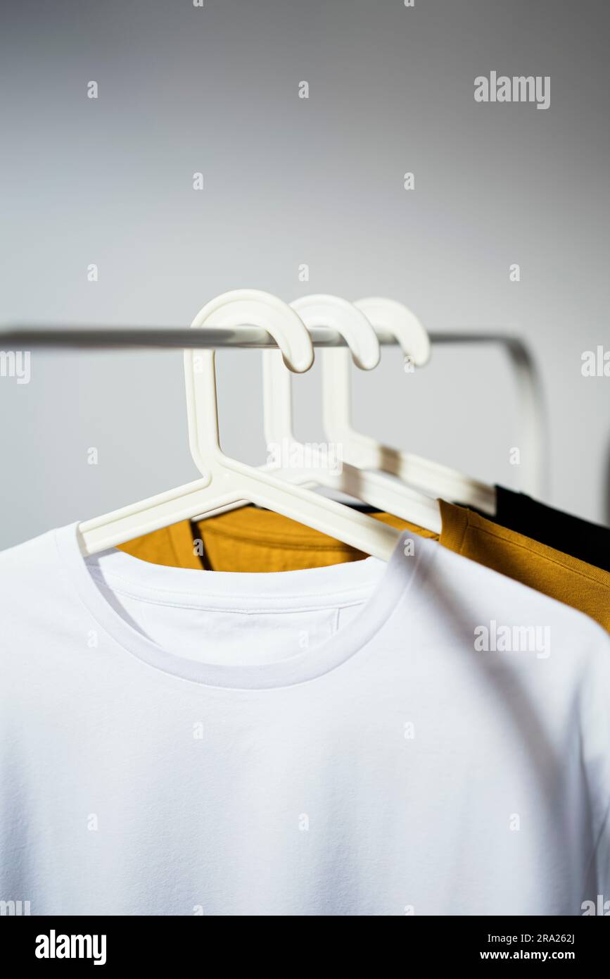 Blank white t-shirt mockup, template on white palstic hanger displayed on white cloths rack with yellow and black t-shirts Stock Photo