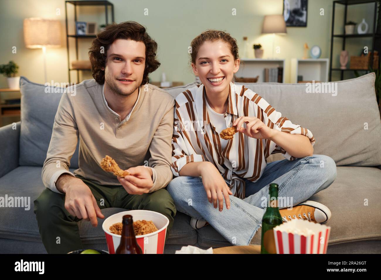 While Viewing Front view portrait of cheerful young couple eating fast food while ...