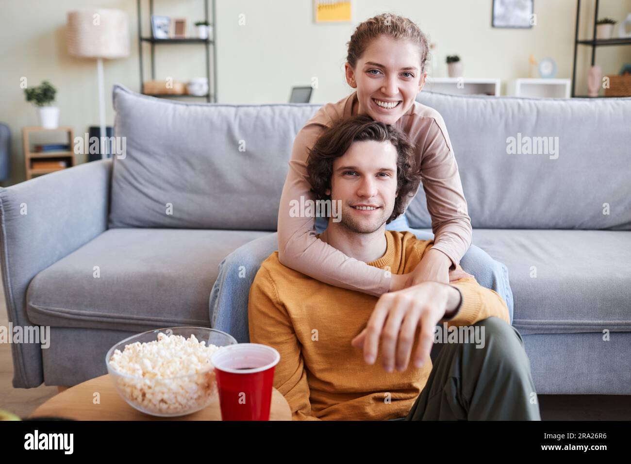 Portrait of carefree young couple watching TV at home and looking at camera, copy space Stock Photo