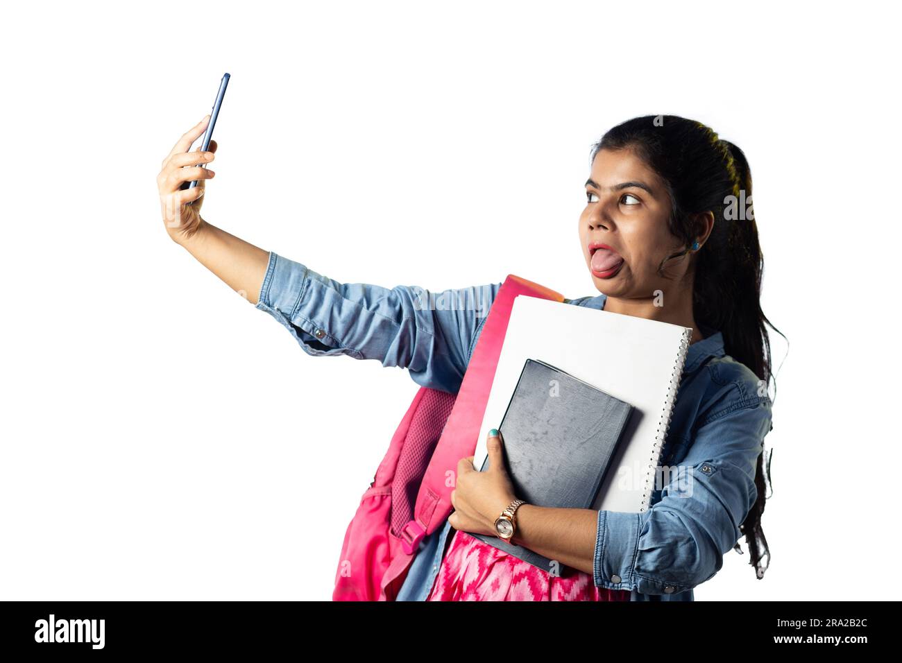 A pretty young Indian modern girl with books in hand taking selfie on white background Stock Photo