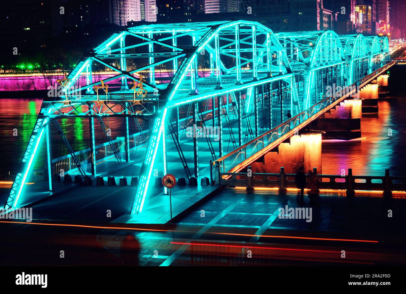 An illuminated bridge on top of a river in a cityscape at night Stock Photo