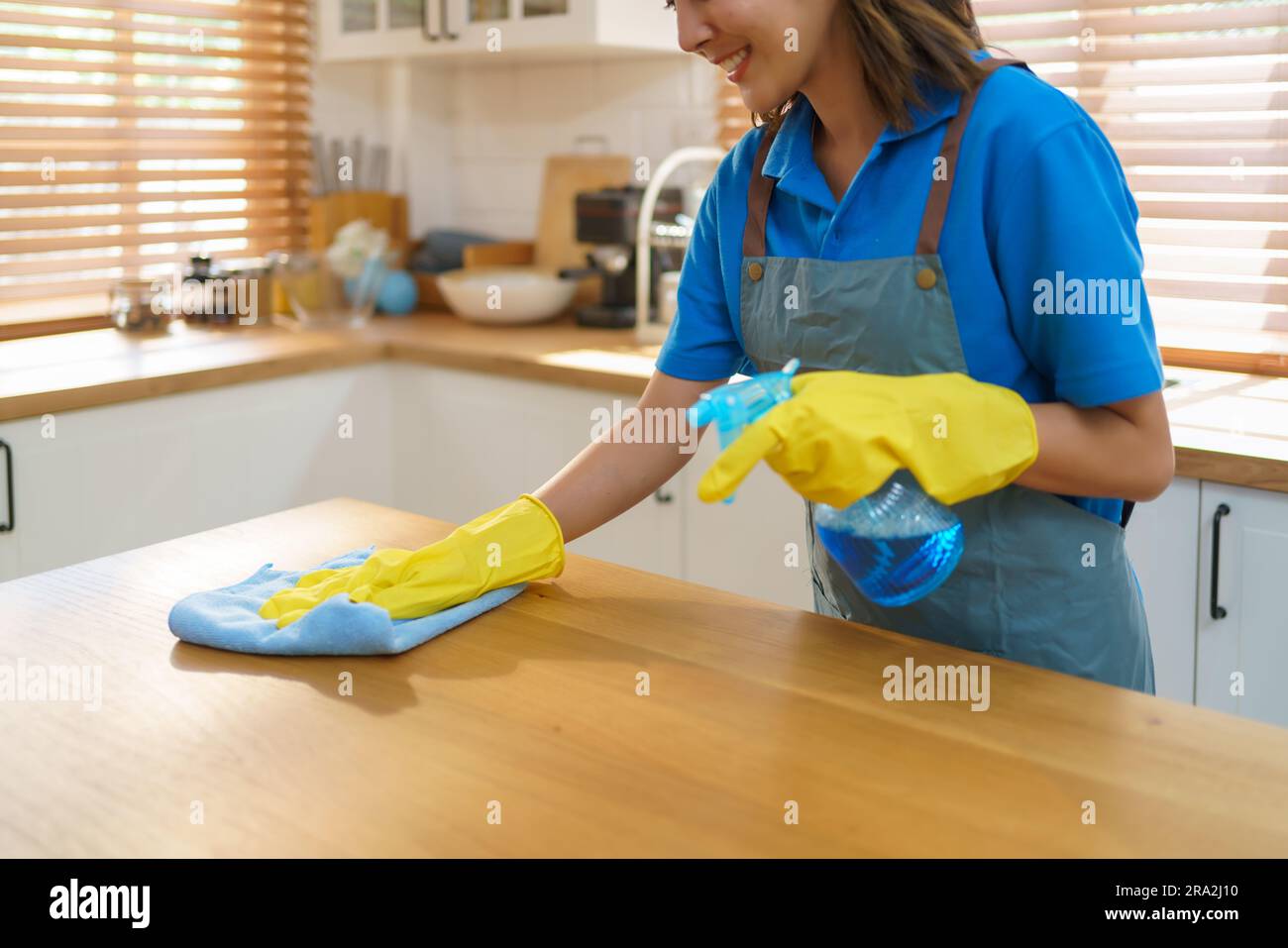 Skillful Asian housewife effortlessly utilizes a tablecloth and sprayer in her kitchen, demonstrating her expertise in creating a clean and inviting s Stock Photo