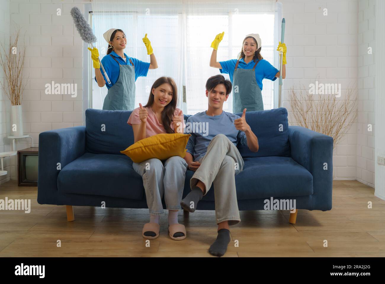 Satisfied Asian homeowner gives a thumbs-up, expressing delight and approval for the exceptional cleaning service provided by the diligent Asian maid Stock Photo