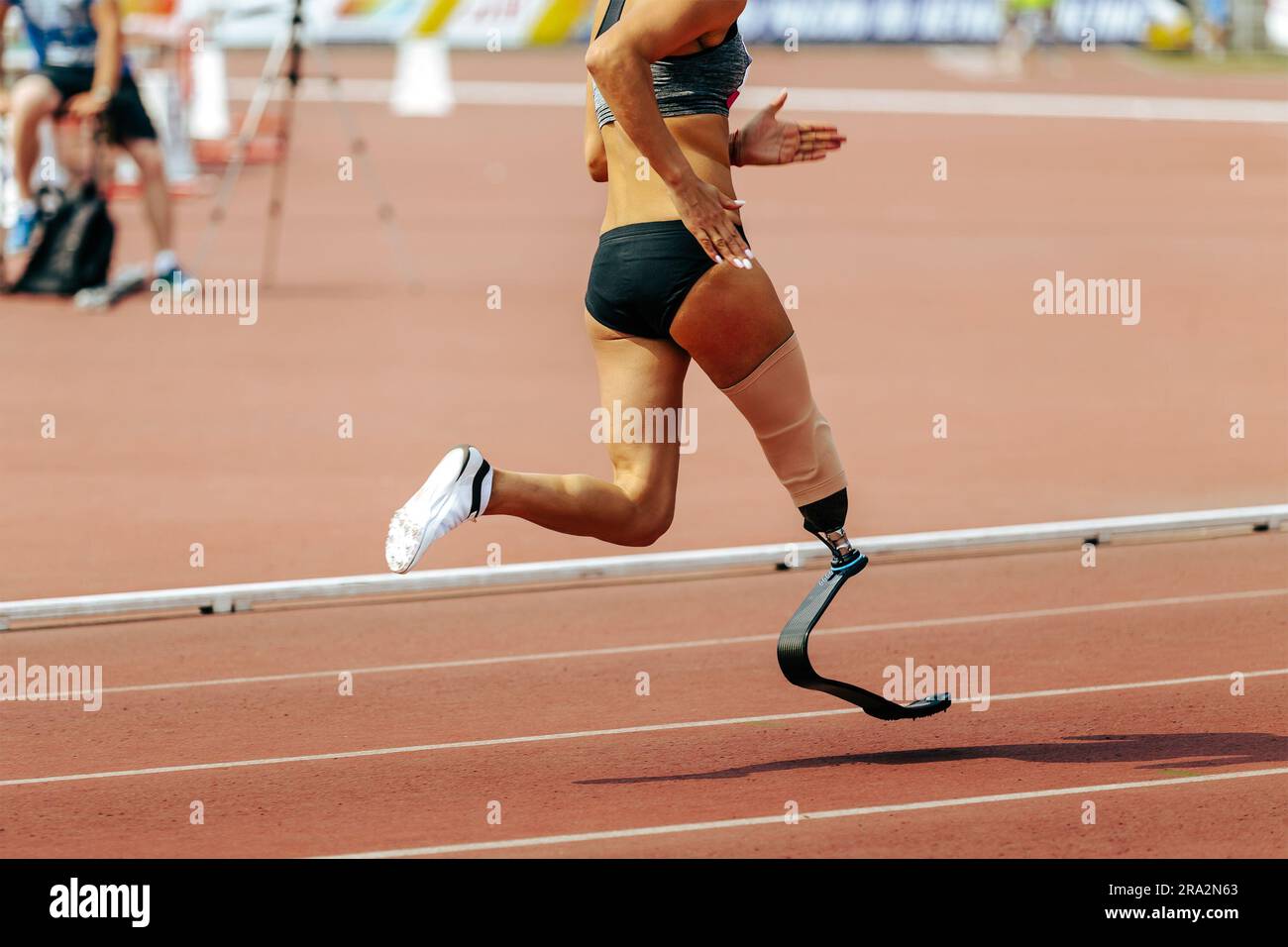 Young woman with prosthetic leg crouching for sports race on footpath stock  photo