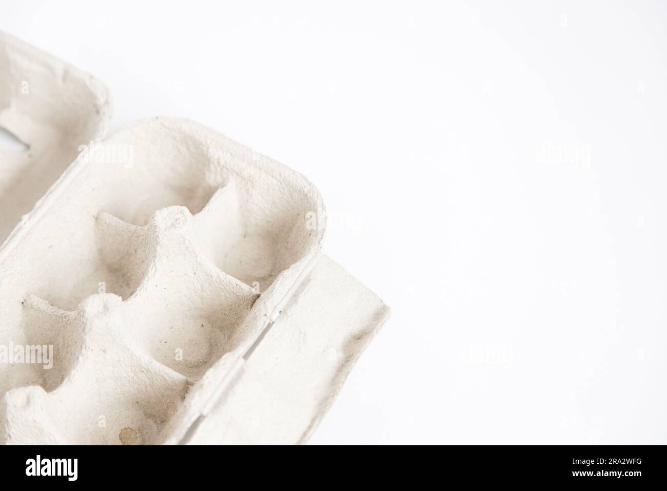 Detail of empty and open recycled cardboard egg carton in the corner of the image on a white background. Close up and copy space. Stock Photo